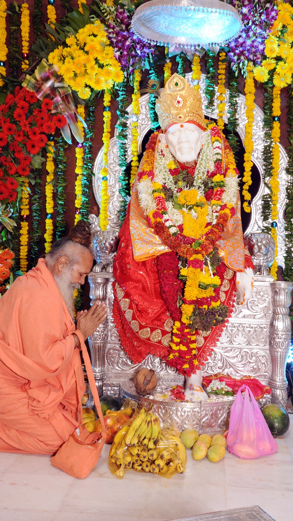 Devotee praying beside Sai Baba murti decorated with flowers and offerings