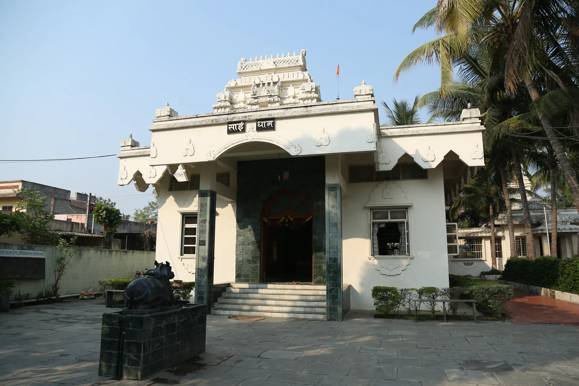 White Saidham Mandir building with steps, shikhara, and a saffron flag
